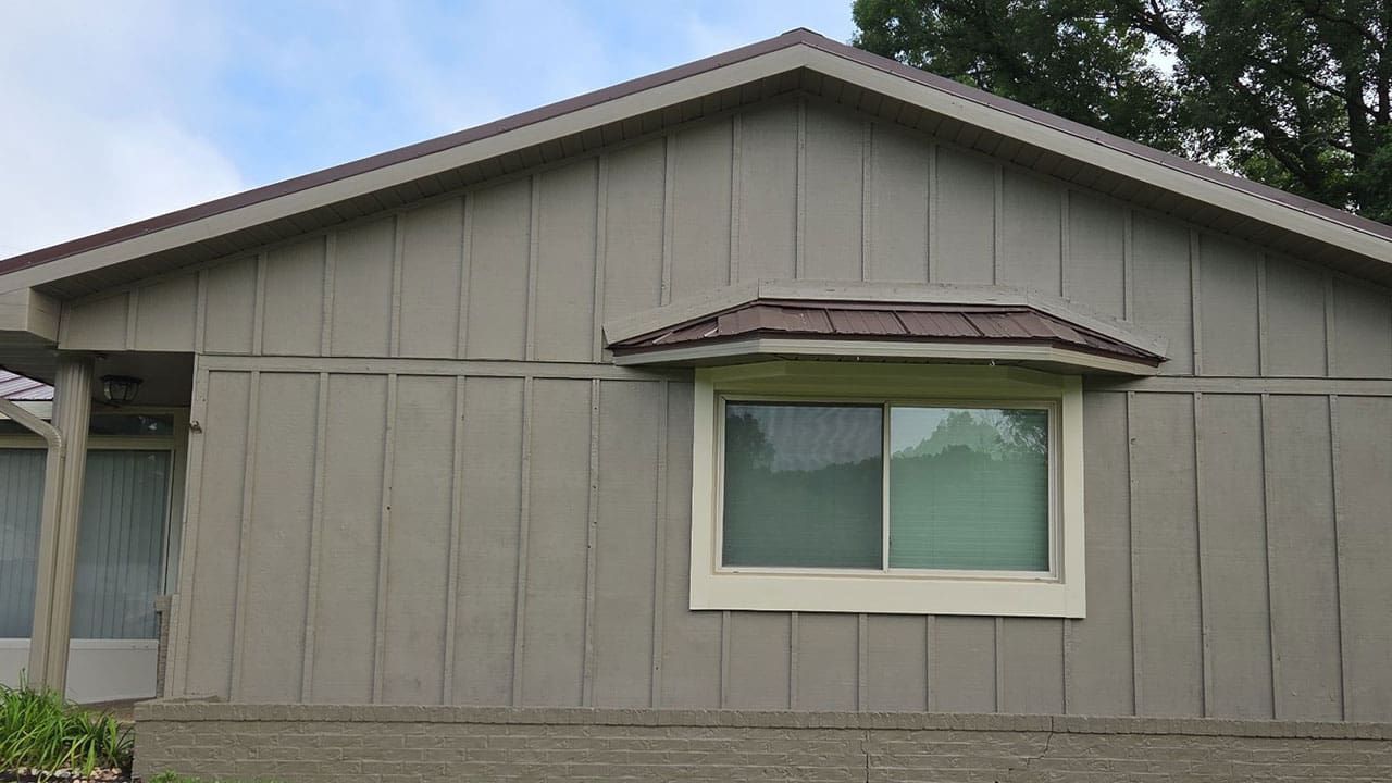 After exterior house painting project featuring fresh light sage green siding update with dark roof trim and modern window casing