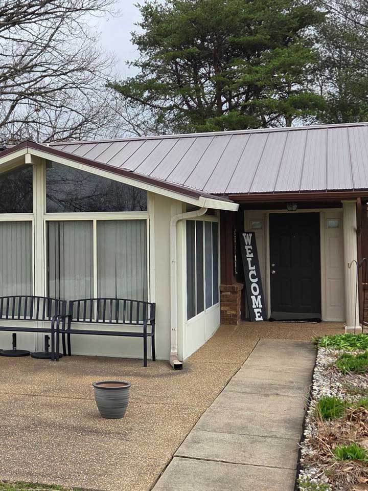 Before front porch exterior repaint in Oakland City IN showing a black front entry door beside enclosed sunroom windows and metal roof