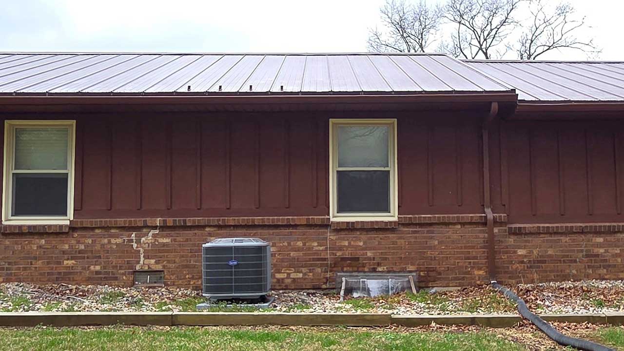 Before rear exterior repaint in Oakland City IN showing faded dark brown vertical siding and unpainted brick wall